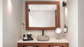 A bathroom with a wooden vanity, a round mirror, and a small potted plant.