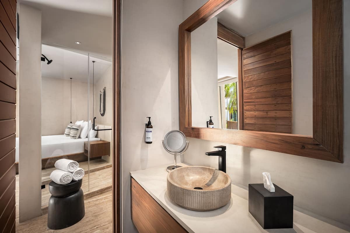 Un baño moderno con un lavamanos redondo, un espejo grande y una mesita de noche con toallas.