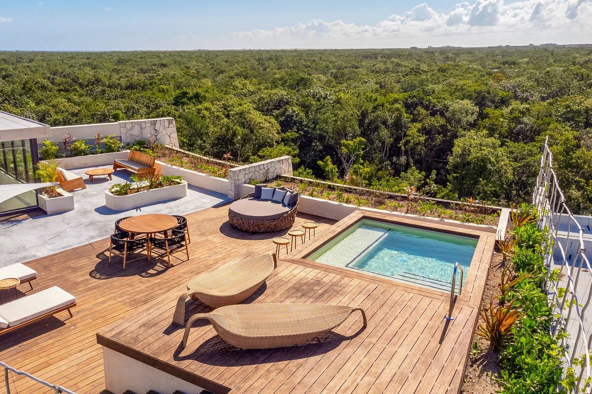Un área de piscina en la azotea con sillones, zona de estar y vistas del bosque circundante.