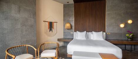 A modern hotel room with a large bed, two wicker chairs, a small round table, and a bench.