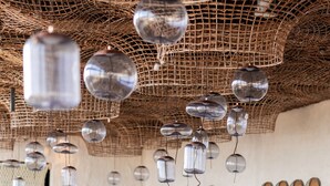 A restaurant with wooden tables and chairs, hanging spherical light fixtures, and wine glasses on the tables.