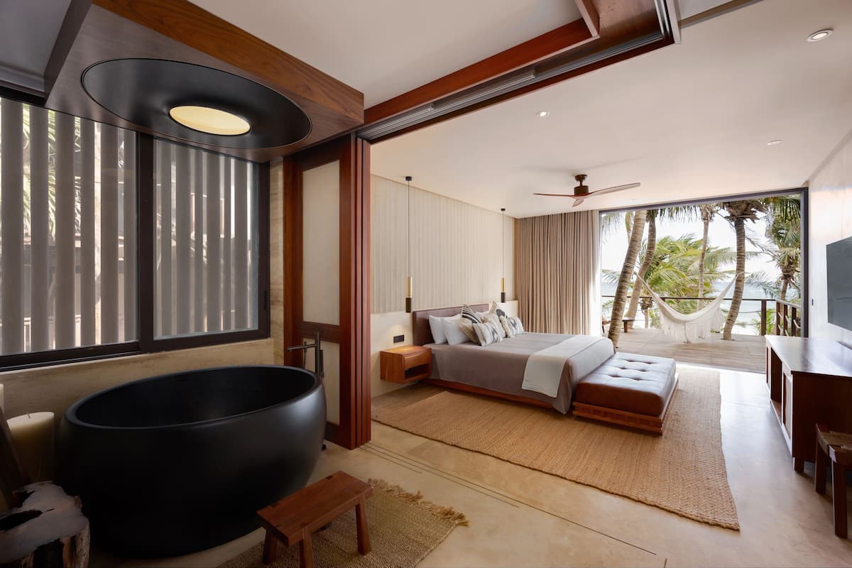 Un dormitorio moderno con una bañera grande, una cama con vistas a palmeras y un balcón.