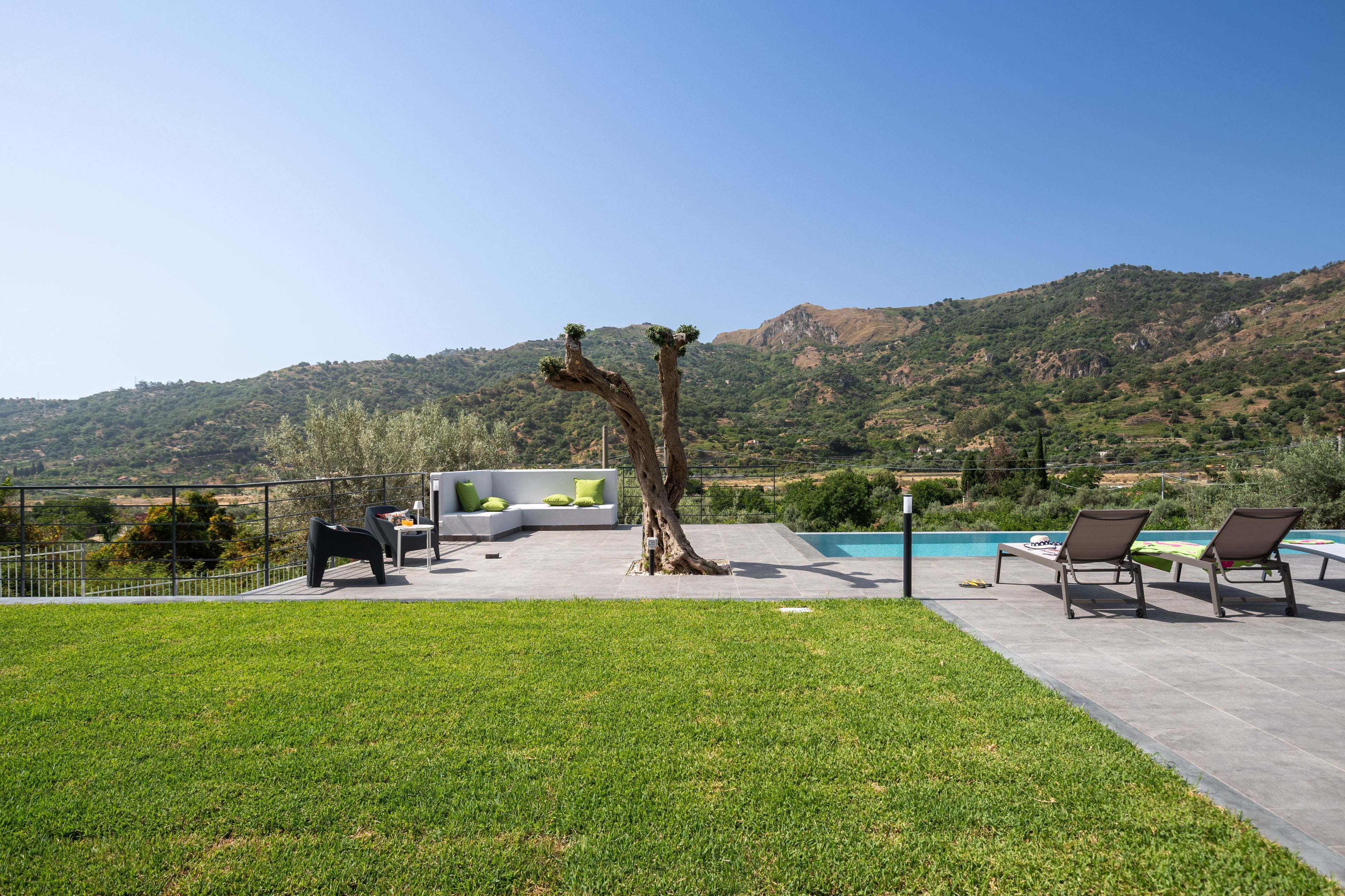 Ein moderner Außenbereich mit Pool, einem Baum und Blick auf eine hügelige Landschaft.