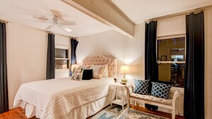 Ein Schlafzimmer mit einem großen Bett, einem Nachttisch, einer Bank, einem Deckenventilator und einem Fenster mit Vorhängen.