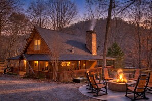 Une cabane en rondins avec une cheminée en pierre, une véranda avec des chaises et un foyer extérieur.