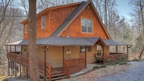 A cabin with a wooden exterior, a porch, and a deck.