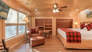 A cozy wooden cabin room with a bed, a sofa, a small table, and a TV mounted on the wall.