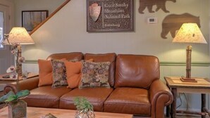 A brown leather sofa with patterned cushions, a framed sign for Great Smoky Mountains National Park, and two table lamps.