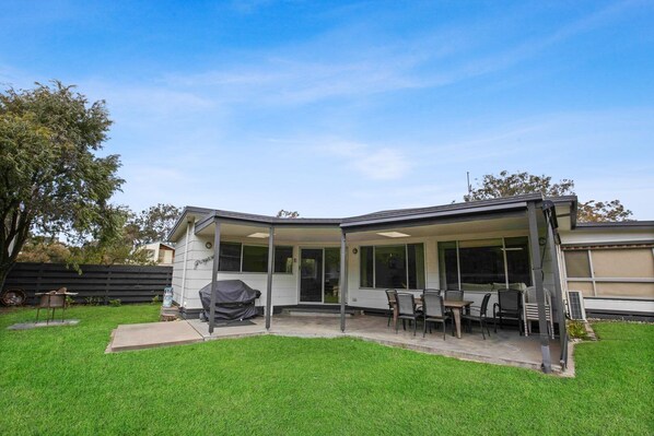 A modern house with a covered patio, a barbecue grill, and a dining area with outdoor furniture.