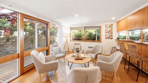 A modern interior with a round table, six chairs, a kitchen area, and large windows. - Bancroft Haven: Nestled above the marina boasting views across Bancroft Bay (Metung)