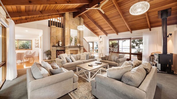 A spacious living room with a high ceiling, a fireplace, and a large window. - Bancroft Haven: Nestled above the marina boasting views across Bancroft Bay (Metung)