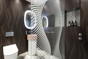 Ein modernes Badezimmer mit einem einzigartigen, geometrischen Wanddesign, einer Duschkabine aus Glas und einer weißen Toilette.