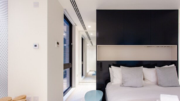 Ein modernes Hotelzimmer mit einem großen Bett, einem Nachttisch und Blick auf den Flur.