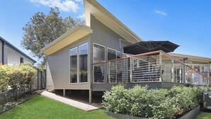 A modern house with a covered outdoor area, a staircase, and a well-maintained lawn. - Karinyah - Panoramic Waterfront Views (Summerland Point)