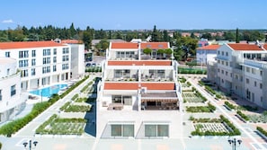 Un hôtel à plusieurs étages doté d’une piscine sur le toit, entouré de jardins aménagés et d’autres bâtiments.