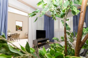 Een moderne woonkamer met een flatscreen televisie, een eethoek met stoelen en een potplant.