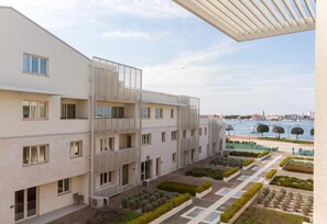 Een modern meerlaags gebouw met balkons, een binnentuin met beplanting, en een uitzicht op een waterlichaam en boten in de verte.
