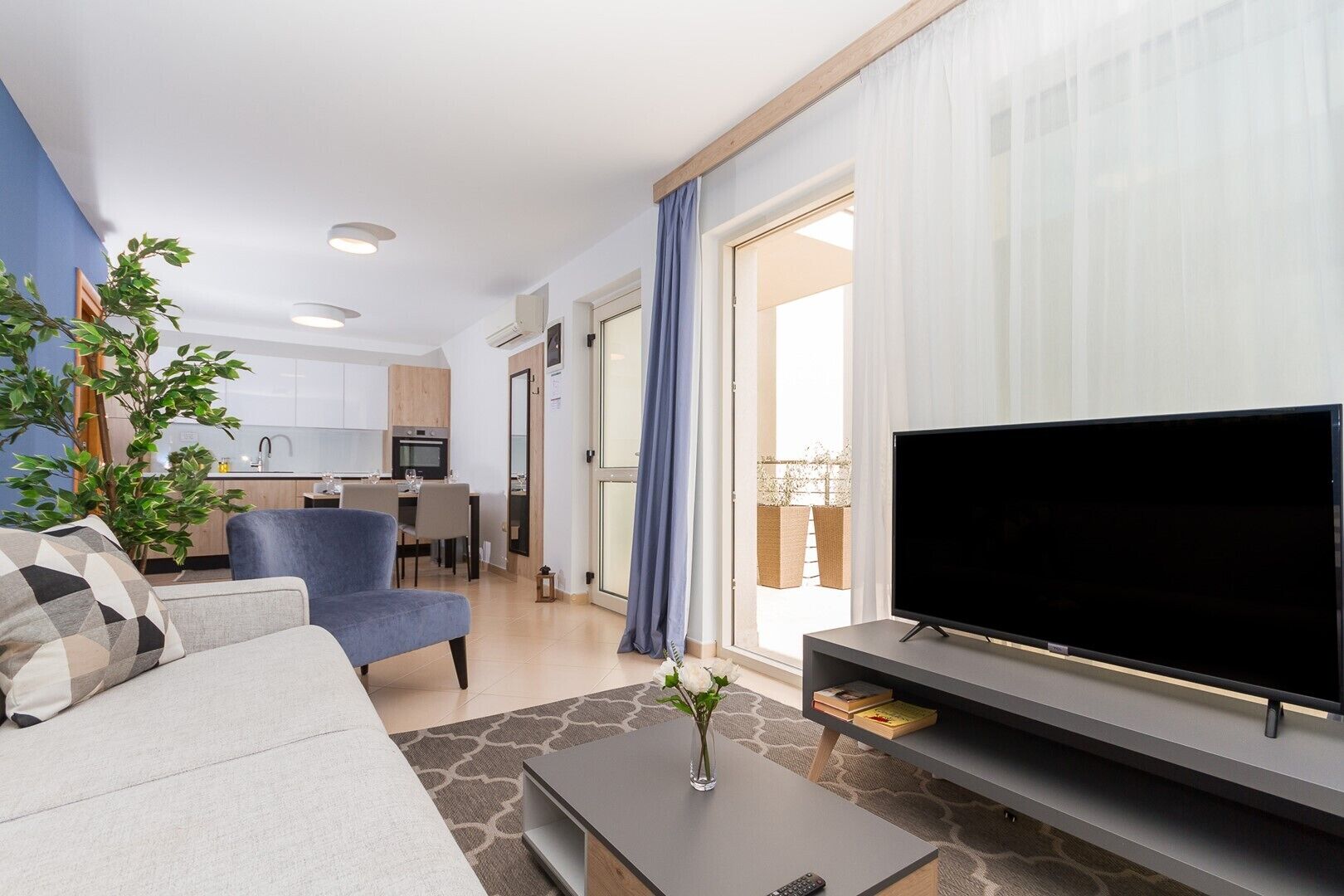 Un salon moderne avec un canapé, un téléviseur, une table basse et, au fond, un coin repas.
