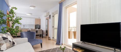 A modern living room with a sofa, a TV, a coffee table, and a dining area in the background.