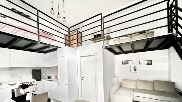 Ein modernes Loft-Apartment mit Küche, Essbereich und Wohnbereich. Es verfügt über eine Galerie mit Treppe, einer Couch und einem Couchtisch.