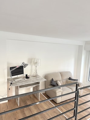 Un soggiorno moderno con pavimento in legno, un divano bianco, un tavolino in vetro, una scrivania con un computer e una lampada.