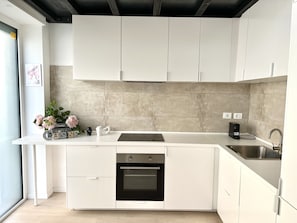 Una cucina moderna con mobili bianchi, forno integrato e lavello in acciaio inossidabile.