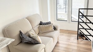 Ein Wohnzimmer mit einem beigefarbenen Sofa, Holzboden und Blick durch eine Glastür.