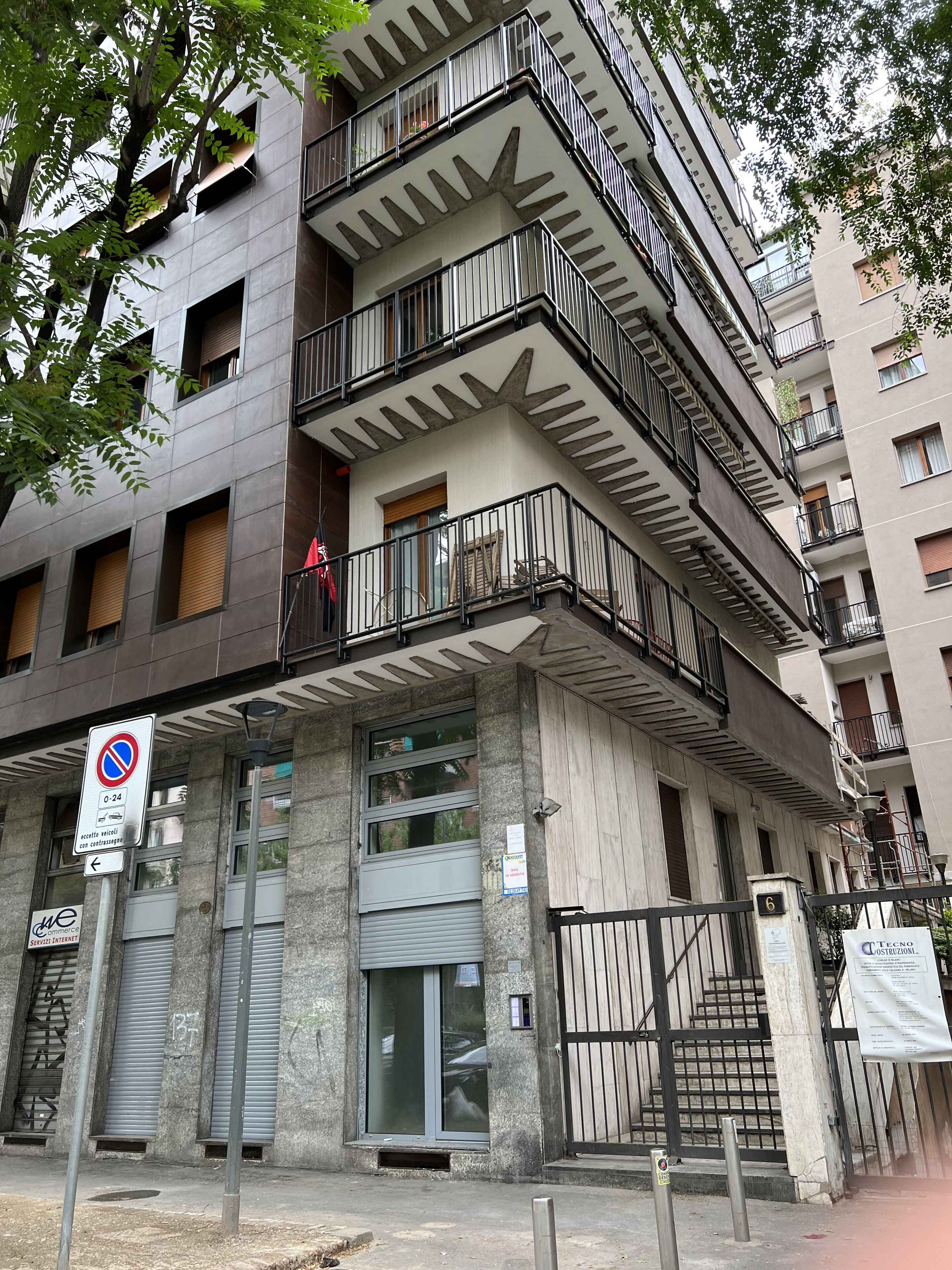 Un edificio a più piani con balconi, un ingresso carrabile con cancello e un segnale che indica divieto di parcheggio.