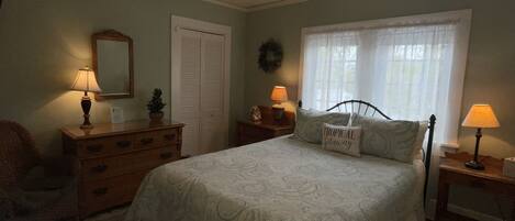 Une chambre à coucher comprenant un lit, un ventilateur de plafond, une fenêtre avec des rideaux, une commode et deux lampes de chevet.