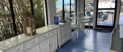 A room with a large window, a white cabinet, a wicker table, and a chair.