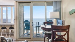 Une pièce dotée d’une porte-fenêtre coulissante donnant sur un balcon avec vue sur l’océan. On y trouve une table, deux chaises et une lampe.
