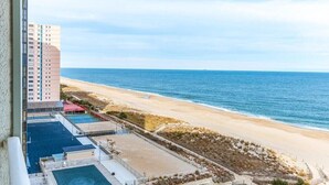 Vue sur la plage depuis un immeuble de grande hauteur, avec une piscine et un sentier menant à la plage.