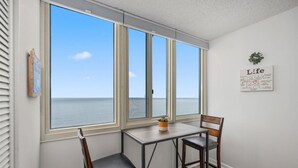 Una habitación con vista al océano, una pequeña mesa con dos sillas y una pared con un cartel.