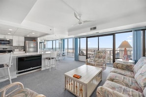 Enjoy a panoramic city view from the large window in this spacious living area with a kitchen, seating area, and ceiling fan.