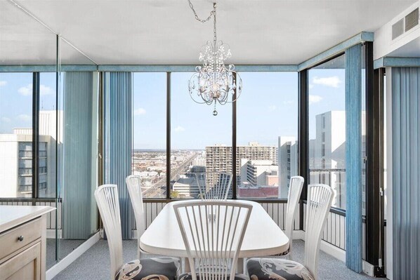 Panoramic city views from a large window, complemented by a central table and chandelier.