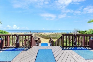 A wooden deck leading to a pool with a view of the beach and ocean.