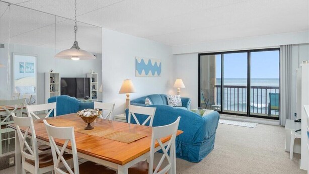 Una sala de estar moderna con comedor, un sofá azul y un ventanal con vista al océano.