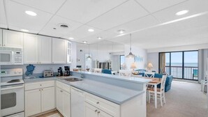 Una cocina moderna con armarios blancos, una isla grande y un comedor con vista al océano.