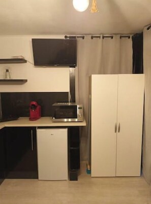Una cocina compacta con microondas, refrigerador pequeño y un armario.