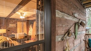 L’intérieur d’un chalet rustique, avec un revêtement extérieur en bois, un ventilateur de plafond, un canapé et une table agrémentée de coussins.
