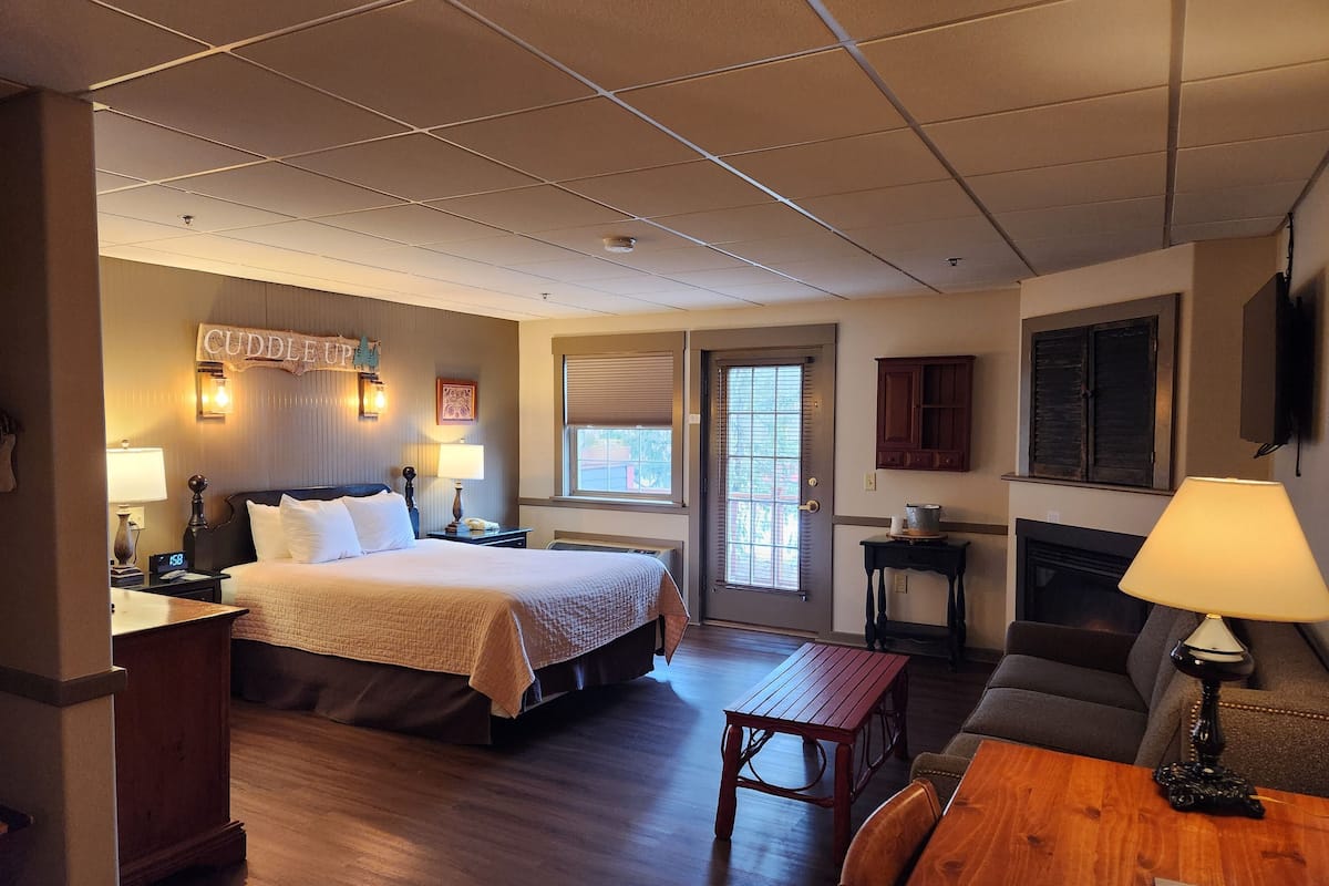 A hotel room with a bed, bedside table, lamp, wooden floor, and a small table with chairs.