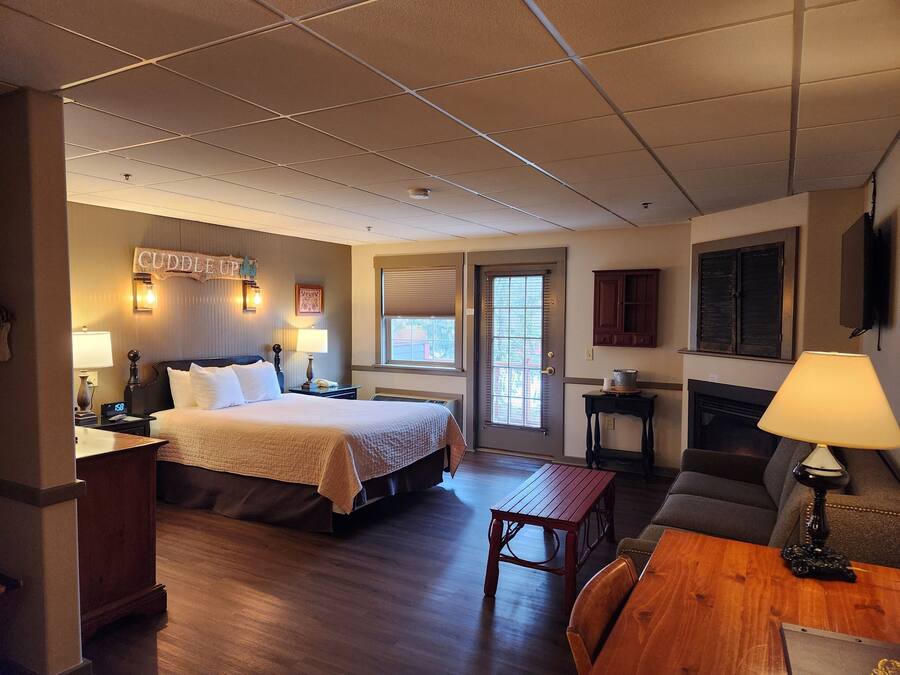 A hotel room with a bed, bedside table, lamp, wooden floor, and a small table with chairs.
