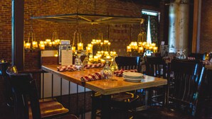 L’intérieur d’un restaurant avec un mur en briques, des luminaires suspendus et des tables en bois dressées pour le service.