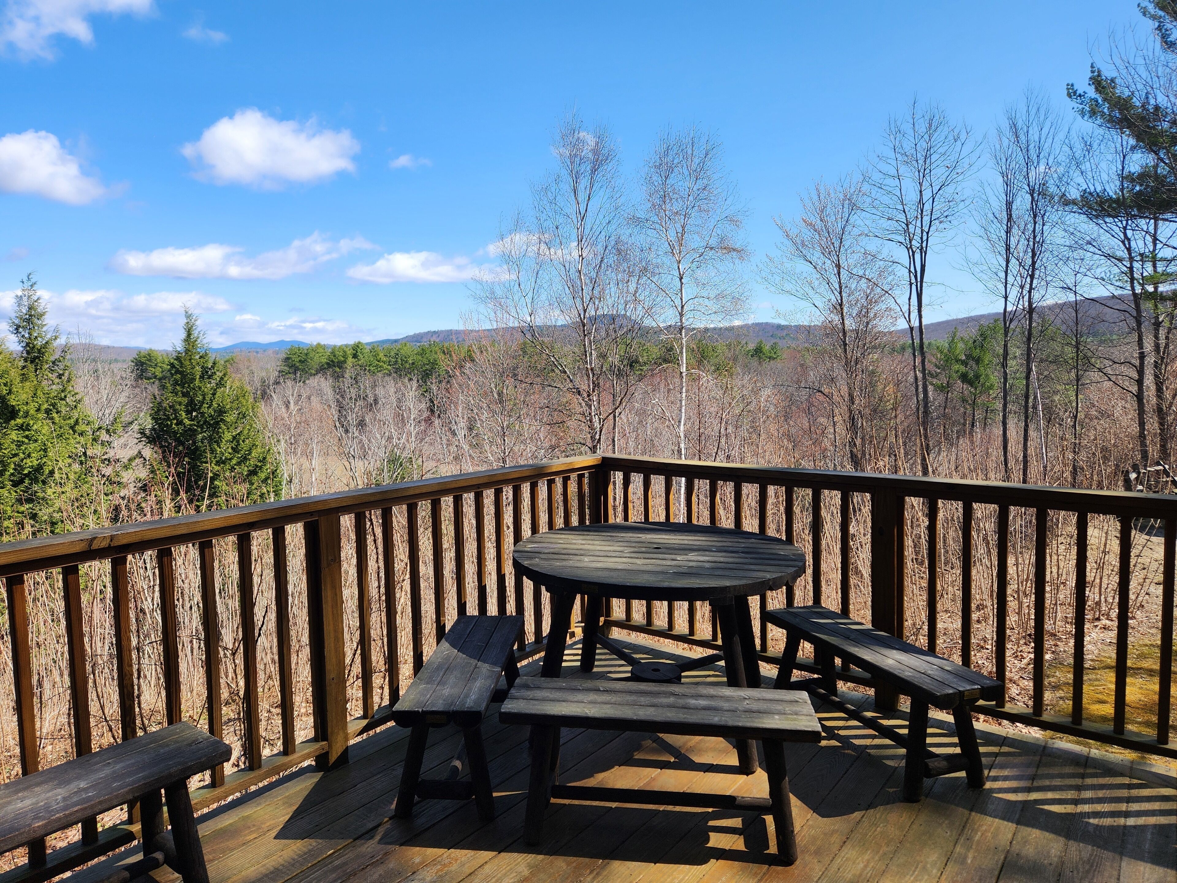A wooden deck with picnic tables and benches, overlooking a forested landscape with mountains in the distance.