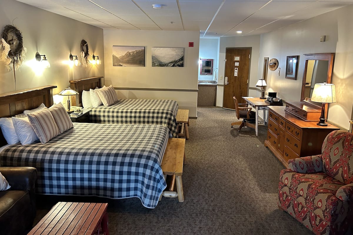 A hotel room with two beds, a desk, a chair, and a dresser.