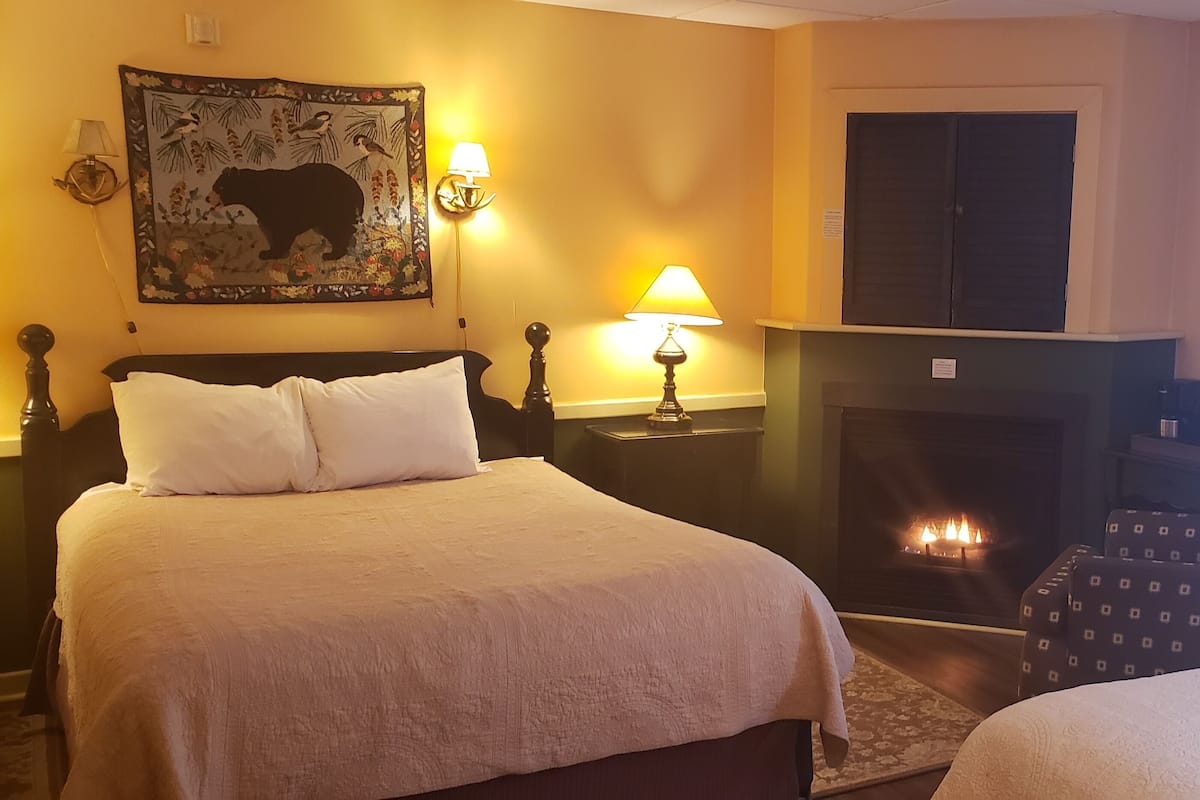 A hotel room with two beds, a fireplace, a wall-mounted lamp, and a painting.