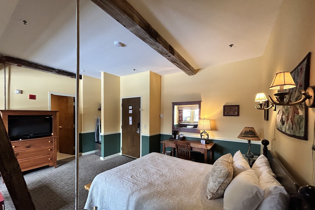 A hotel room with a bed, a desk, a television, and a mirror.