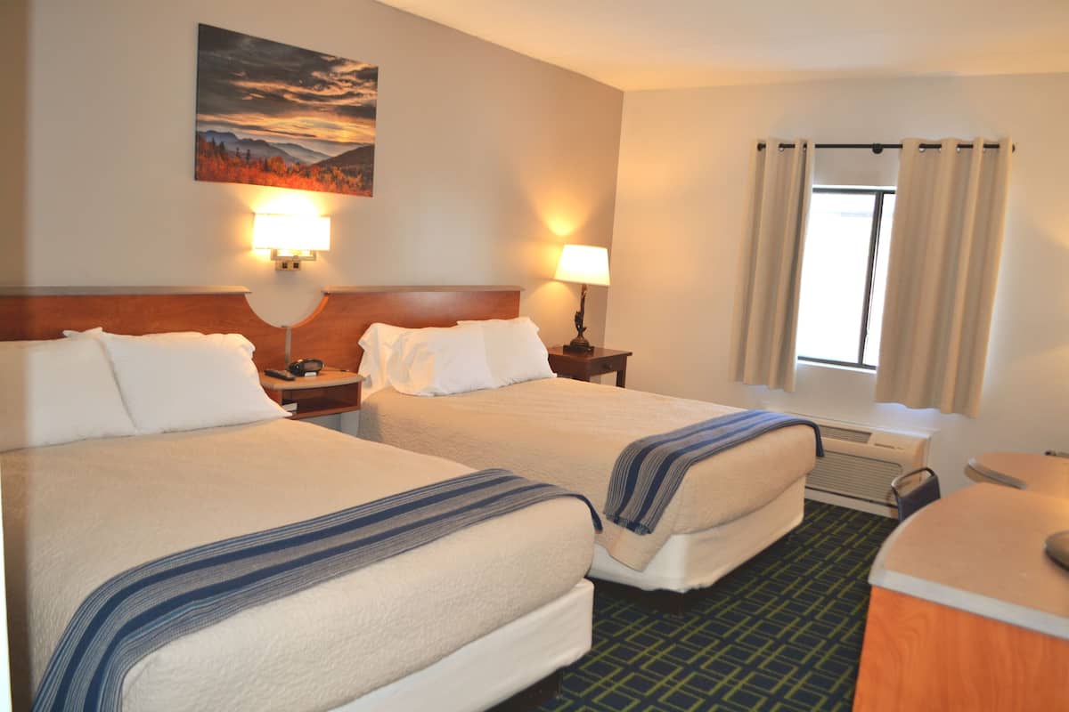 A hotel room with two beds, a desk, a chair, a lamp, and a window with curtains.