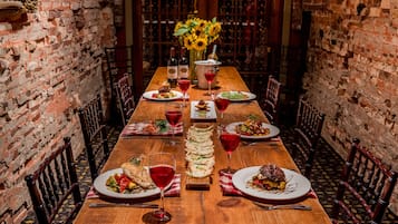 Una larga mesa de madera dispuesta para una comida, con platos de comida, copas de vino tinto y un jarrón con girasoles en el centro.