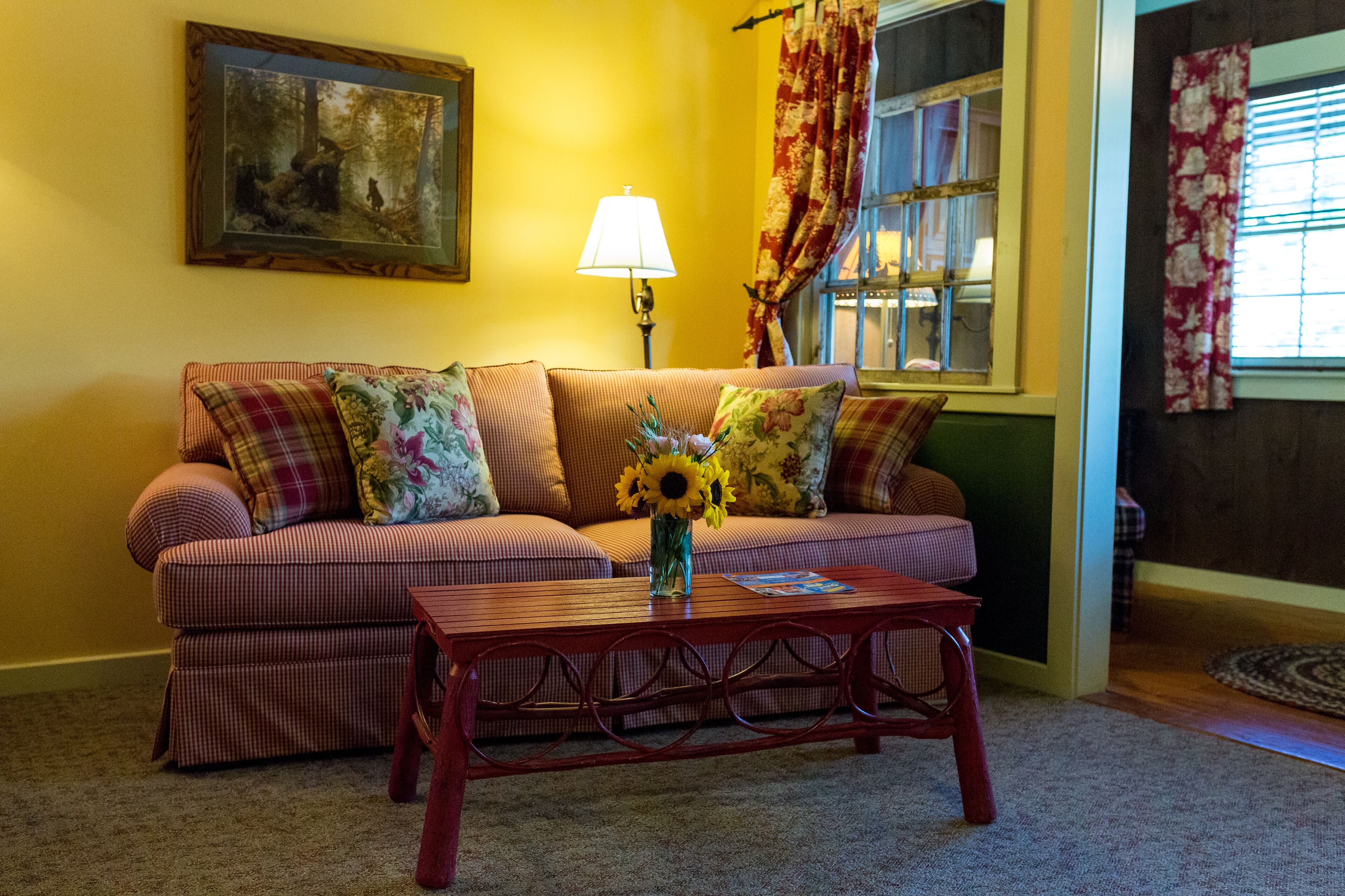 A living room with a sofa, a coffee table with a vase of flowers, a lamp, and a painting on the wall.